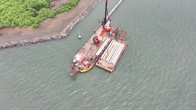 aerial view of the process of installing a giant sea wall by a large drilling machine on the north coast of Java Island