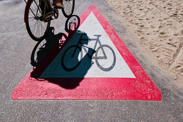 Cyclist Passing Over a Bike Path Triangle Sign near Beach. Bicycle Lane Warning Sign with Rider...