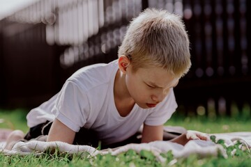 A boy with hearing aids plays on the grass while engaging with gadgets - drawing on a tablet and...