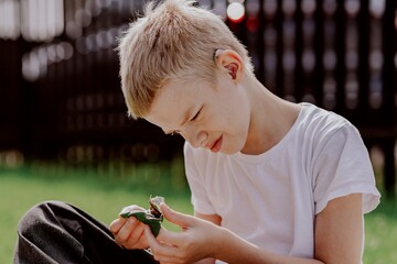 A boy with hearing aids gazes curiously at a snail on a leaf, capturing a magical childhood moment...