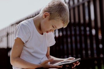 A boy with hearing aids plays on the grass while engaging with gadgets - drawing on a tablet and...