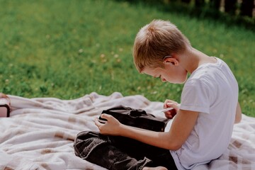 A boy with hearing aids plays on the grass while engaging with gadgets - drawing on a tablet and...