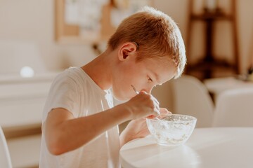 A boy with hearing aids enjoys a bowl of warm porridge in a sunlit kitchen, radiating pure...