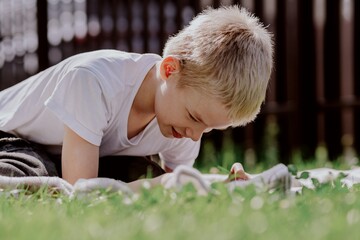 A boy with hearing aids plays on the grass while engaging with gadgets - drawing on a tablet and...
