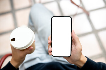 Hands holding coffee and white screen smartphone using application or social media as sits on bench.