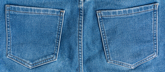 Fototapeta premium Close-up of rear view of two pockets decorated with stitches of casual comfortable blue jeans made from cozy denim fabric material used as warm everyday clothing for cold season of autumn or winter