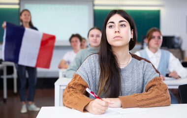 Geography lesson in school class - teacher talks about France, holding a flag in his hands
