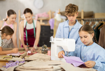 Girl sews on a sewing machine. A boy watches and learns