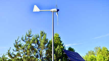 Solar panels with wind turbine on blue sky. Concept of clean energy. Green technology for future. 