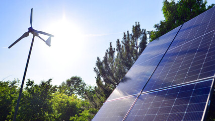 Solar panels with wind turbine on blue sky. Concept of clean energy. Green technology for future. 