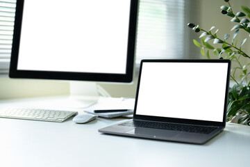 Modern white desk with a large desktop monitor and a laptop