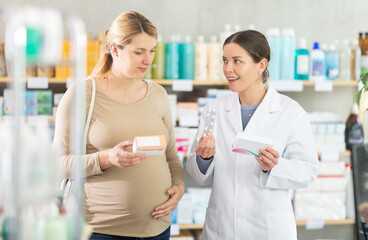 Fototapeta premium Professional young female pharmacist with smile providing detailed advice on safe medication options during pregnancy, helping interested expectant mother understand usage and precautions..
