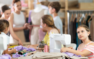 Girl learns to sew on sewing machine in class. Children learn to make a pattern with their teacher