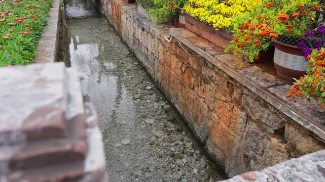  A quiet stream flowing through a narrow stone-lined water channel in Lijiang Old Town. This iconic feature of Naxi architecture reflects the town&rsquo;s peaceful rhythm and centuries-old water system.