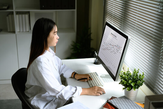 Focused woman reviewing business profit graphs on desktop monitor in a home office