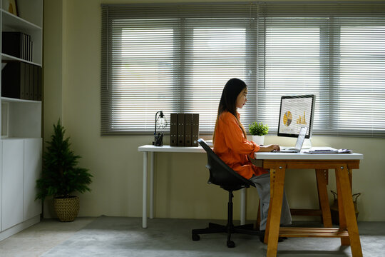 Young woman working at desk, reviewing charts and graphs on a computer monitor