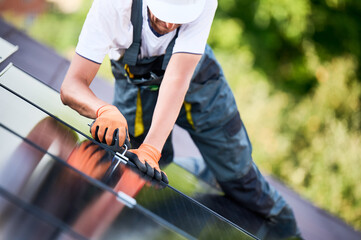 Worker building photovoltaic solar panel system on rooftop of house. Close up of man engineer in...