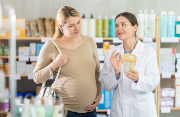 Pregnant woman choose infant formula in pharmacy, examine packaging. Assortment of pharmacy...