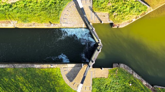 Aerial view canal lock balancing water levels. Overhead shot sluice gate controlling flow. Top-down perspective hydraulic system adjusting passage. High-angle frame navigational lock regulating