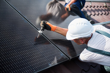 Workers building photovoltaic solar panel system on rooftop of house. Close up of men technicians...