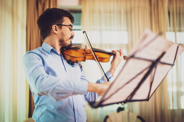 Man playing violin at home. He is practicing for live performance.