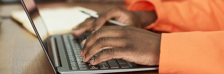 Black man typing on laptop keyboard wearing orange uniform, participating in educational program in...