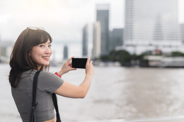 Happy solo asian woman on vacation taking photo of Bangkok with smartphone. Smiling blogger enjoys...