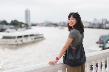Happy solo Southeast Asian woman and teenager blogger. world travel explorer wait for boat. local...