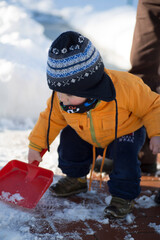 An adorable toddler dressed in a warm orange jacket and a striped hat stands in a snowy landscape,...