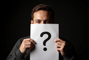 Man hiding behind paper sheet with question mark on dark background