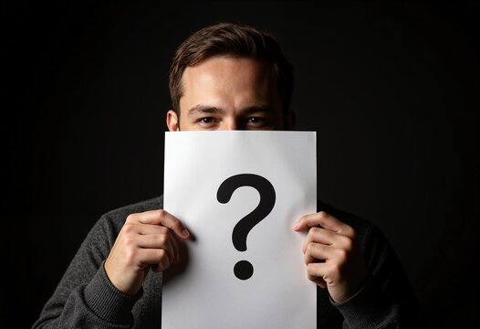 Man hiding behind paper sheet with question mark on dark background