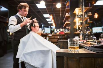 Close-up photo of a glass of whiskey. High-quality barbershop offering drinks to customers. Glass with alcohol on the background of hairstylist making haircut.