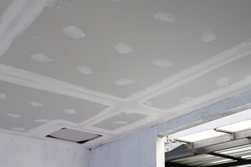 Obraz premium Interior renovation progress building smooth gypsum board ceiling edges. Plastering complete on ceilings showing precise work. Electrical wire visible reflecting effort towards finishing