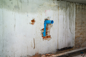 Old dirty concrete wall with broken blue pipe during house renovation. Grunge background showing...