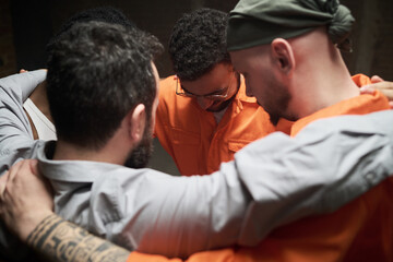 Group of diverse men standing close together in circle embracing shoulders participating in group therapy session in prison setting showing support and unity