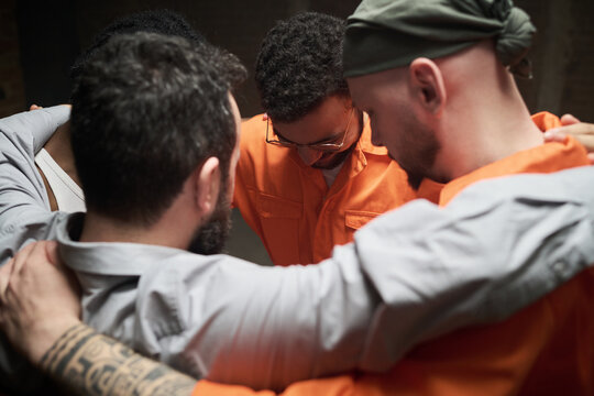 Group of diverse men standing close together in circle embracing shoulders participating in group therapy session in prison setting showing support and unity