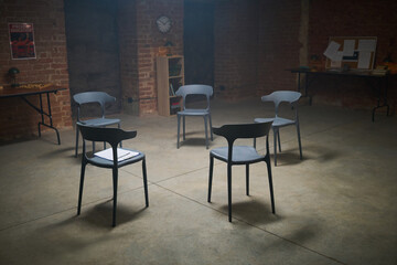 Empty chairs arranged in circle in spacious room with exposed brick walls, suggesting group therapy or support meeting setting, notebook resting on one chair, no people present