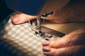 Close-up of hands guiding fabric through sewing machine with blue thread and light