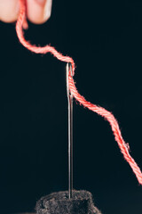 Close-up macro photo of red thread being inserted into sewing needle eye