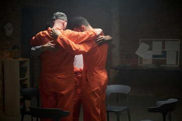 Group of young adult multiethnic men wearing prison uniforms standing in circle embracing each...