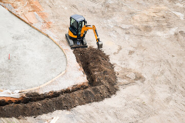 Aerial wide view of excavator digging a curved trench for foundation work at a construction site....