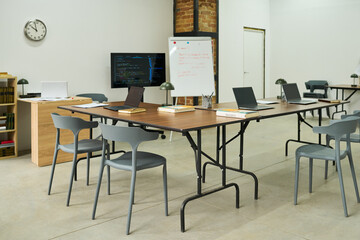 Empty classroom with several laptops, books, and notebooks arranged on tables, whiteboard and monitor displaying educational materials, setting representing prison education environment