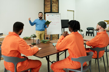 Caucasian middle aged man teaching poetry class to group of young adult men in orange prison...