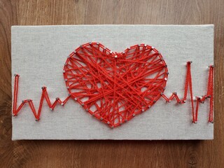 Heart crafted with vibrant red string art displaying heartbeat rhythm on textured canvas surface...