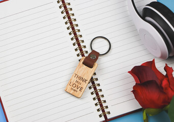 wooden keyring with word "Think less love more" on opened diary  with headphones and red rose  on blue background.
