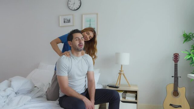 Caucasian husband getting back massage treatment from his wife at home. 