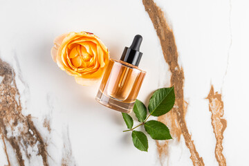 A transparent bottle with a dropper of serum, oil lies on an abstract marble background with the head of a tea rose. Natural moisturizing. top view