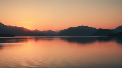 Naklejka premium Serene lake reflecting a distant mountain and colorful sky at sunset, capturing natural beauty in the Lake District.