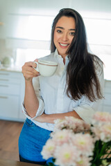 Young woman drinking hot coffee at home in the kitchen.