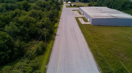 Topdown aerial view of an expansive industrial warehouse surrounded by lush green fields and dense trees, showcasing the contrast between manmade structures and natural landscapes with vibrant textur